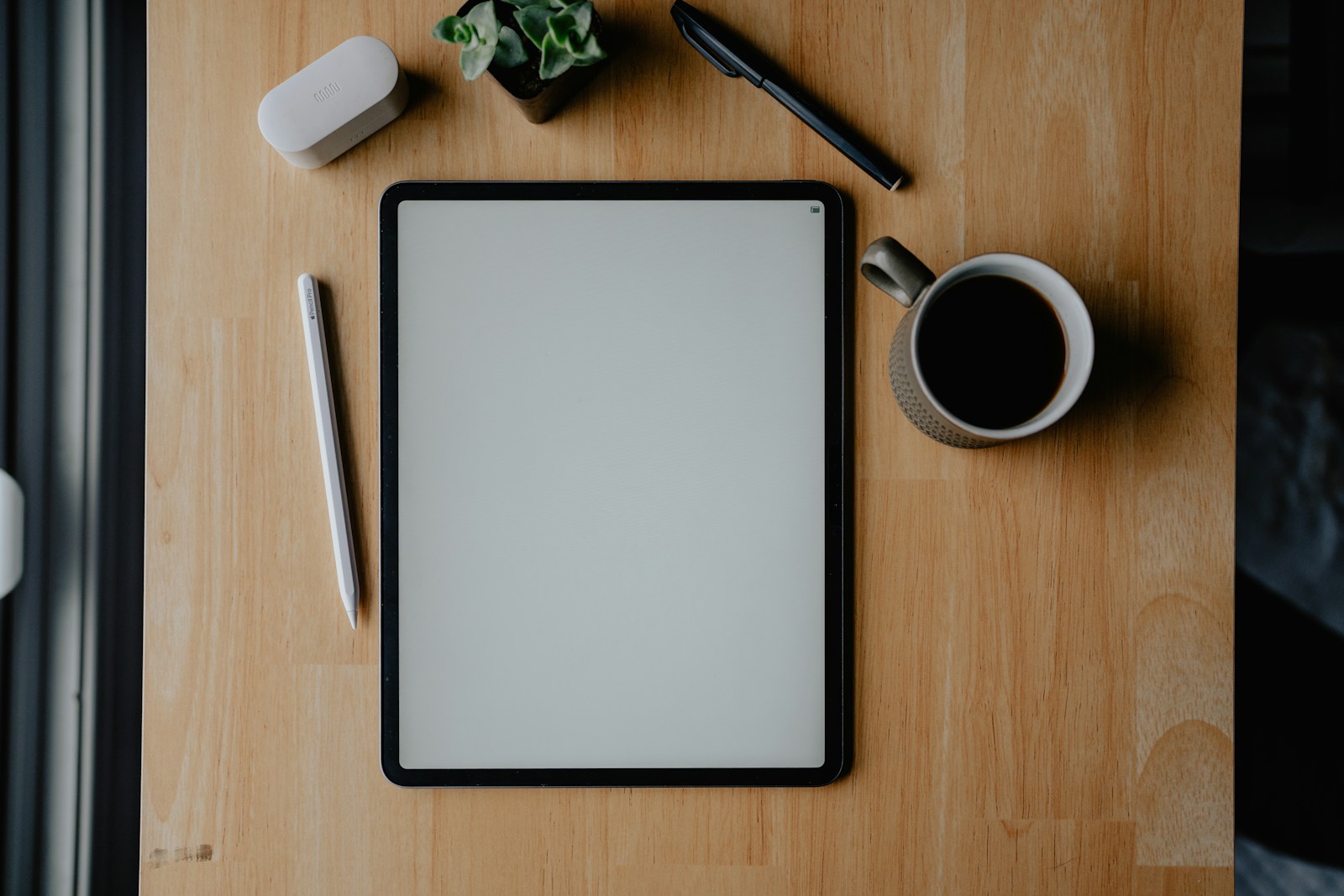 Tablet, accessories, and coffee on a wooden desk.